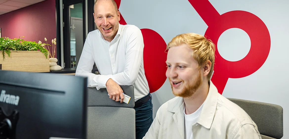 man werkt op computer en tweede man kijkt mee om te controleren opvolgend werkgeverschap